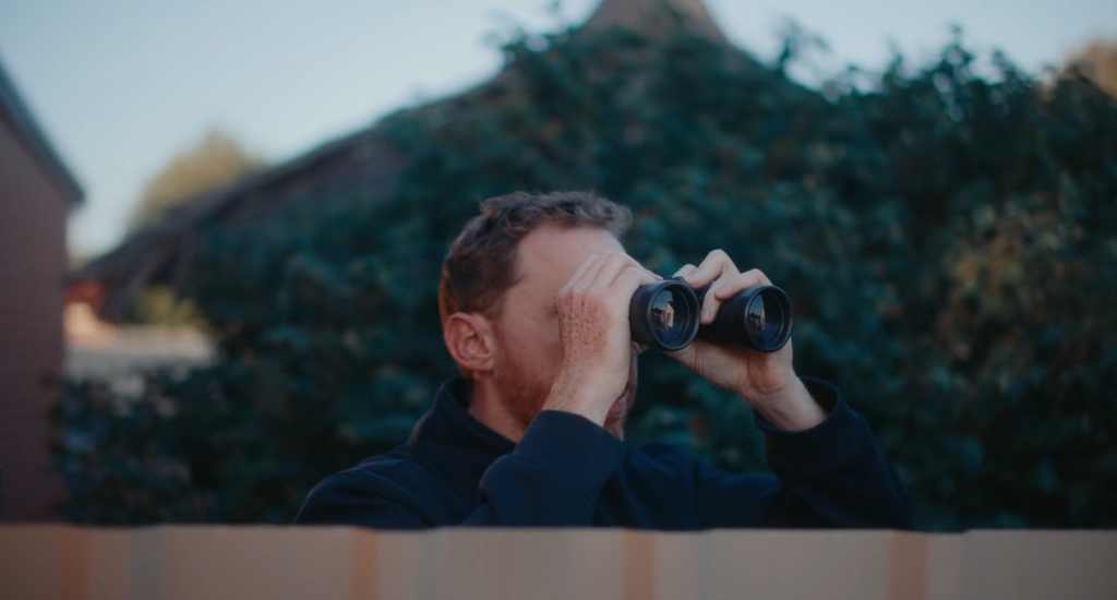 Man looking through binoculars over his fence.